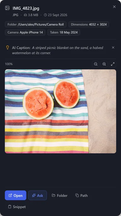 Preview of IMG_4823.jpg with its AI caption: a striped picnic blanket on the sand with a halved watermelon.