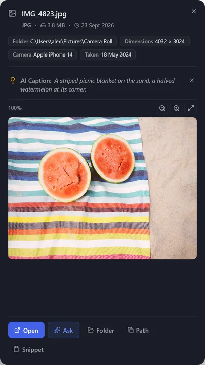 Preview of IMG_4823.jpg with its AI caption: a striped picnic blanket on the sand with a halved watermelon.