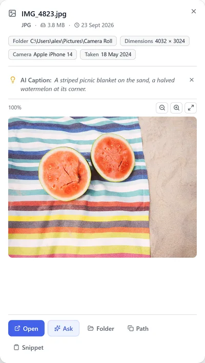 Preview of IMG_4823.jpg with its AI caption: a striped picnic blanket on the sand with a halved watermelon.